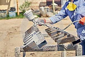 Crop man painting metal detail with paint gun in the backyard