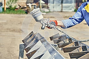 Crop man painting metal detail with paint gun in the backyard