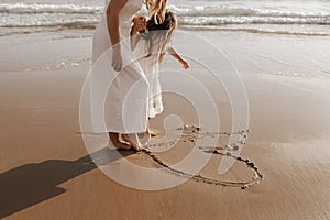 Crop mother and daughter drawing heart on sand