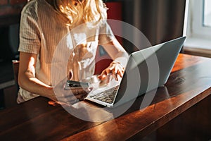 Crop photo of  blonde woman with long hair working on laptop and using mobile phone on kitchen at the home, remote work