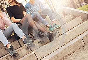 Crop photo of group of friends Millennials students teenagers sitting at city street, friendship, close up focus on feet