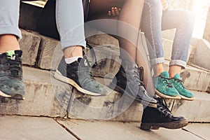Crop photo of group of friends Millennials students teenagers sitting at city street, friendship, close up focus on feet