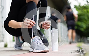 Crop unrecognizable woman runner wearing hygiene protective face mask sitting and tieing shoe rope during workout running in city