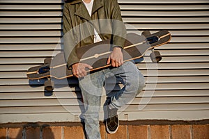 Crop of urban skater man posing for camera with longboard