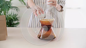 Crop video of a woman putting fine coffee grounds on a paper filter before making pour-over on ground coffee over the paper filter