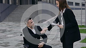Crop view of attractive woman with paper folder coming to disabled man and shaking his hand outdoors. Happy male and