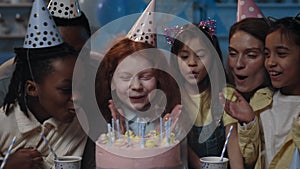 Crop view of diverse children, man and woman blowing candles on cake all together with birthday girl. Happy people and