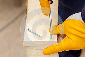 Crop view driving self-tapping screw into chipboard placed on wooden workbench