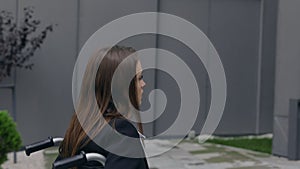 Crop view of female person in suit pushing herself on wheel chair at street. Disabled woman going to work and stopping