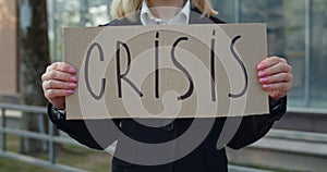 Crop view of female worker showing carton banner with crisis writing. Jobless woman in suit standing at street after