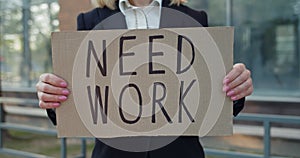 Crop view of female worker showing carton banner with need work writing. Woman searching for job while standing at