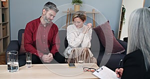 Crop view of married emotional couple make up while sitting at female psychologist office. Husband and wife smiling and