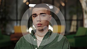 Crop view of millennial guy with stylish haircut looking to camera. Portrait of handsome young man posing while sitting