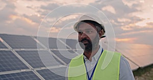 Crop view of mixed raced male engineer in uniform. Bearded man in hard helmet walking at solar power plant for