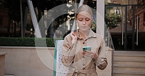 Crop view of pretty blonde hair woman using her smartphone while walking. Millennial attractive girl carrying shopping