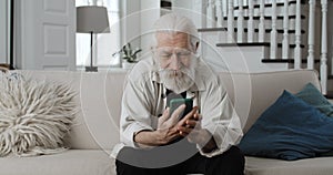 Crop view of senior grey haired grandfather looking at photos while touching phone sreen.Positive bearded male pensioner