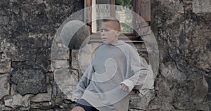 Crop view of teen boy kicking soccer ball with knee. Talanted kid practicing tricks. Old damaged building facade at