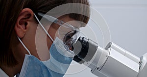 Crop view of young medical female worker looking to microscope. Woman in protective mask and googles examining sample