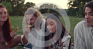 Crop view of young people eatting while sitting on grass and having picnic. Diverse millennial friends smiling and