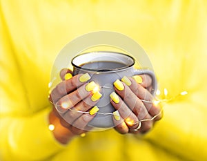 Crop woman with coffee cup in glowing garland