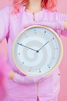 Croped image of young female doctor with office clock  on pink background