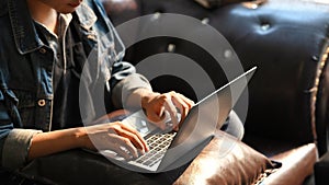 Croped shot male hands typing on laptop keyboard on while sitting on sofa.