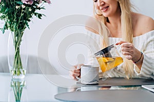 Cropped attractive woman kitchen pouring herb tea teapot. Vase plant. Close up