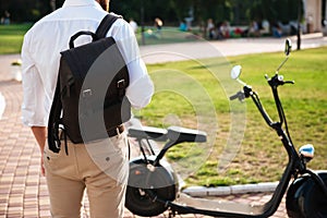 Cropped back view of man with backpack standing near motorbike