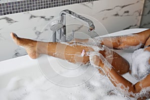 cropped black young woman shaving her sexy legs while taking bath at home, copy space