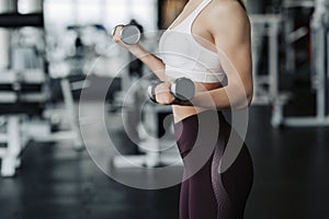 Cropped body close up of young attractive woman in sport clothes holding weight dumbbell doing fitness workout in the gym