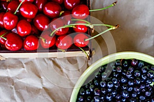 Cropped bowl of blueberries and box, crape of red sweet cherries with tail on craft wrinkled old paper background