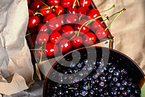 Cropped bowl of blueberries and box, crape of red sweet cherries with tail on craft wrinkled old paper background