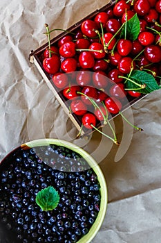 Cropped bowl of blueberries and box, crape of red sweet cherries with tail on craft wrinkled old paper background