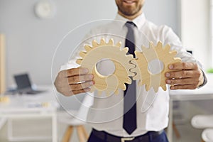 Cropped businessman holding 2 cogwheels that fit perfectly as metaphor for effective business system