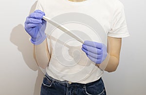 Cropped Caucasian manicurist, nail technician holds file in hands, wearing gloves. White photo