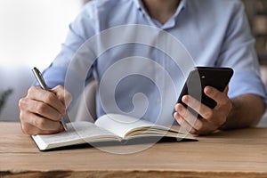 Cropped close up businessman holding smartphone, writing down information