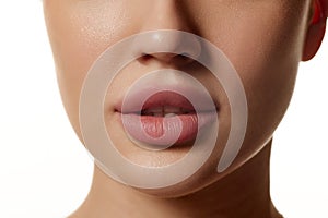 Cropped close-up image of beautiful female face, plump lips with nude lipsticks makeup isolated against white studio