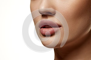 Cropped close-up image of beautiful female face, plump lips with nude lipsticks makeup isolated against white studio
