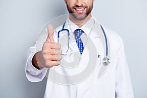 Cropped close up photo of bearded successful young doctor in white uniform, he is standing at the pure white background with