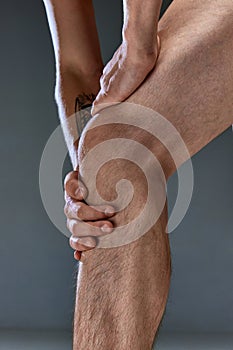 Cropped close up photo of leg of young athletics man touching knee at pain point. Male model posing shirtless Muscular