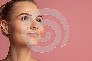 Cropped close-up portrait of young beautiful girl with bun isolated over pink background