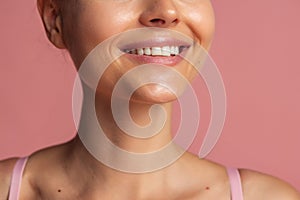 Cropped close-up portrait of young smiling girl isolated over pink background