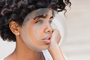 Cropped close-up shot of beautiful young dark skinned woman wearing casual with sad, pensive, reflective look, against white wall