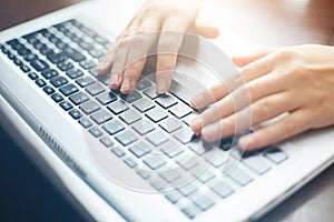 Cropped close up shot of woman`s hands typing on keyboard while chatting using computer laptop sitting at wooden table. Human, lei