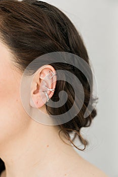 Cropped close-up shot of a young woman with asymmetrical silver ear cuffs. Female with metal ear cuffs, side view