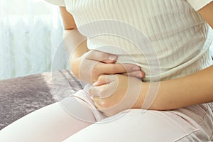 Cropped close up view girl touch stomach suffers from severe ache sitting on sofa