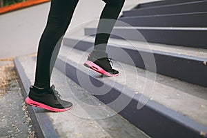 Cropped close up of woman legs in sportswear, black and pink sneakers doing sport exercises, climbing on stairs outdoors