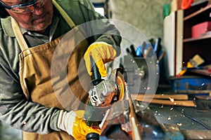 Cropped closeup horizontal image of adult worker man manufacturing in his workshop. Indoor shot of senior male grinding with