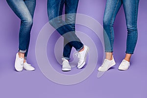 Cropped closeup photo of three people`s legs wearing denim dark blue jeans trousers pants standing on the floor isolated