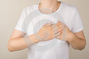 Cropped closeup photo of woman in white t-shirt holding her hands on heart on isolated grey background